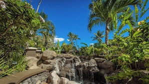 Un jardin tropical avec une cascade, des palmiers et un sentier en pierre.