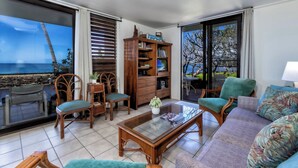 Un salon avec vue sur la mer, une bibliothèque en bois, un canapé et un coin repas avec des chaises.