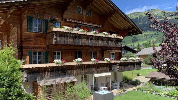 En træchalet med altaner, en terrasse og udsigt over det omkringliggende landskab.
