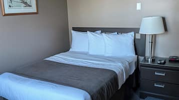 A hotel room with a bed, a nightstand, a lamp, and a framed picture on the wall.