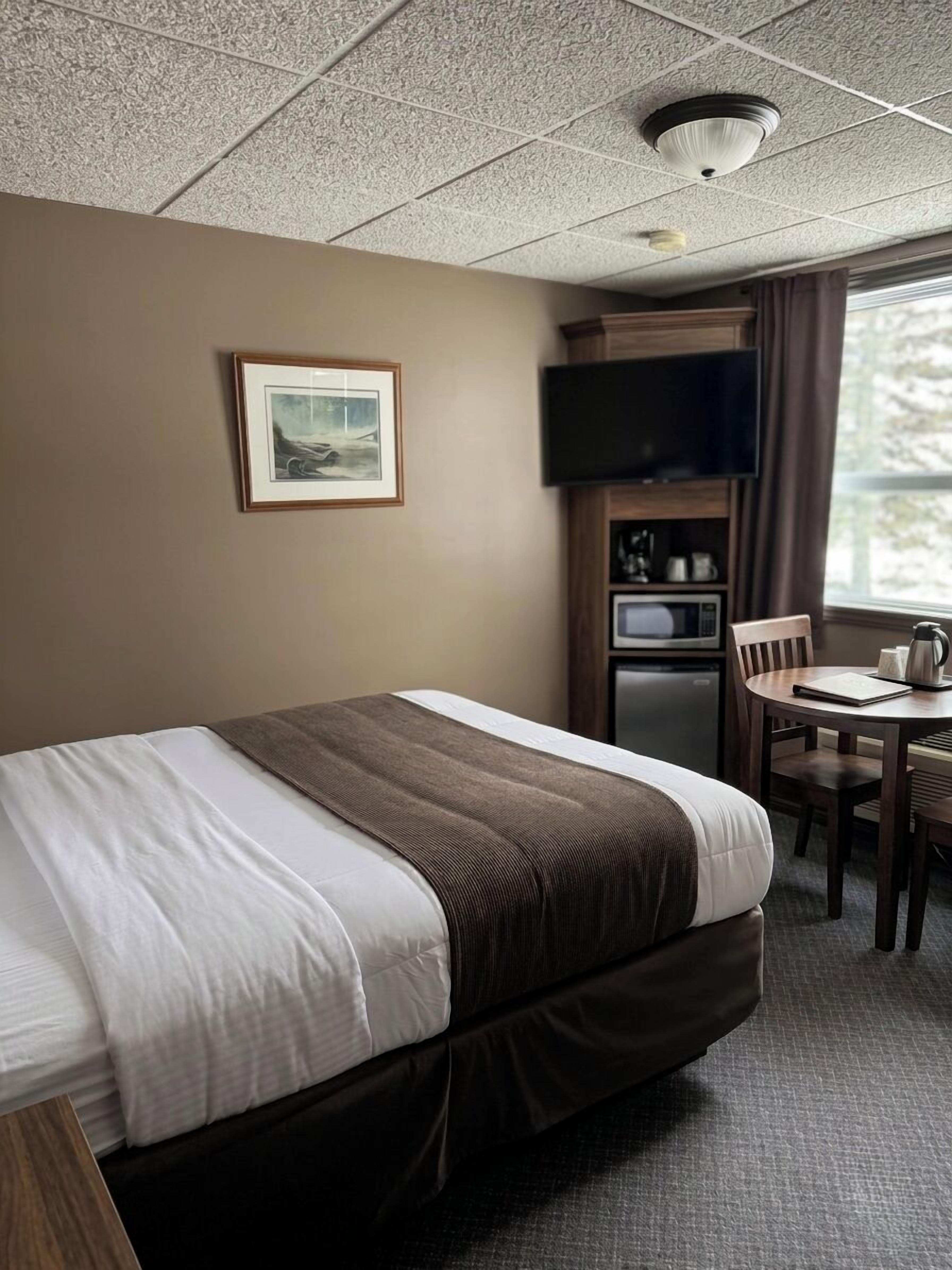 Habitación de hotel con cama, televisión, una mesita con una silla y ventana.