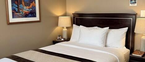 Habitación de hotel con una cama grande, una mesita de noche, una lámpara, un cuadro enmarcado y un cartel en la pared.