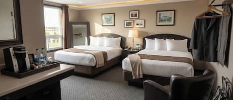 A hotel room with two beds, a desk with a coffee maker, a chair, and a coat rack.