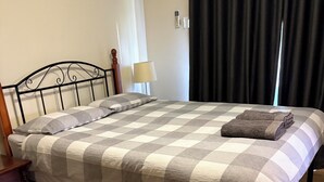Un lit avec une couvre-lit à carreaux, une table de chevet avec une lampe et une petite table en bois placée à côté du lit.