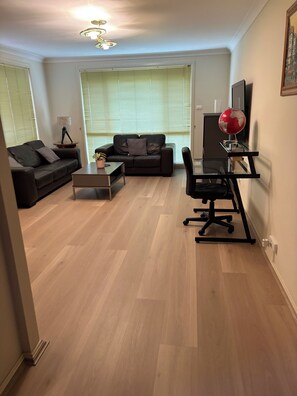 A living room with a sofa, a coffee table, a desk with a chair, a globe, and a lamp. - 4 BEDROOM HOUSE IN CECIL HILLS NSW (Cecil Hills)