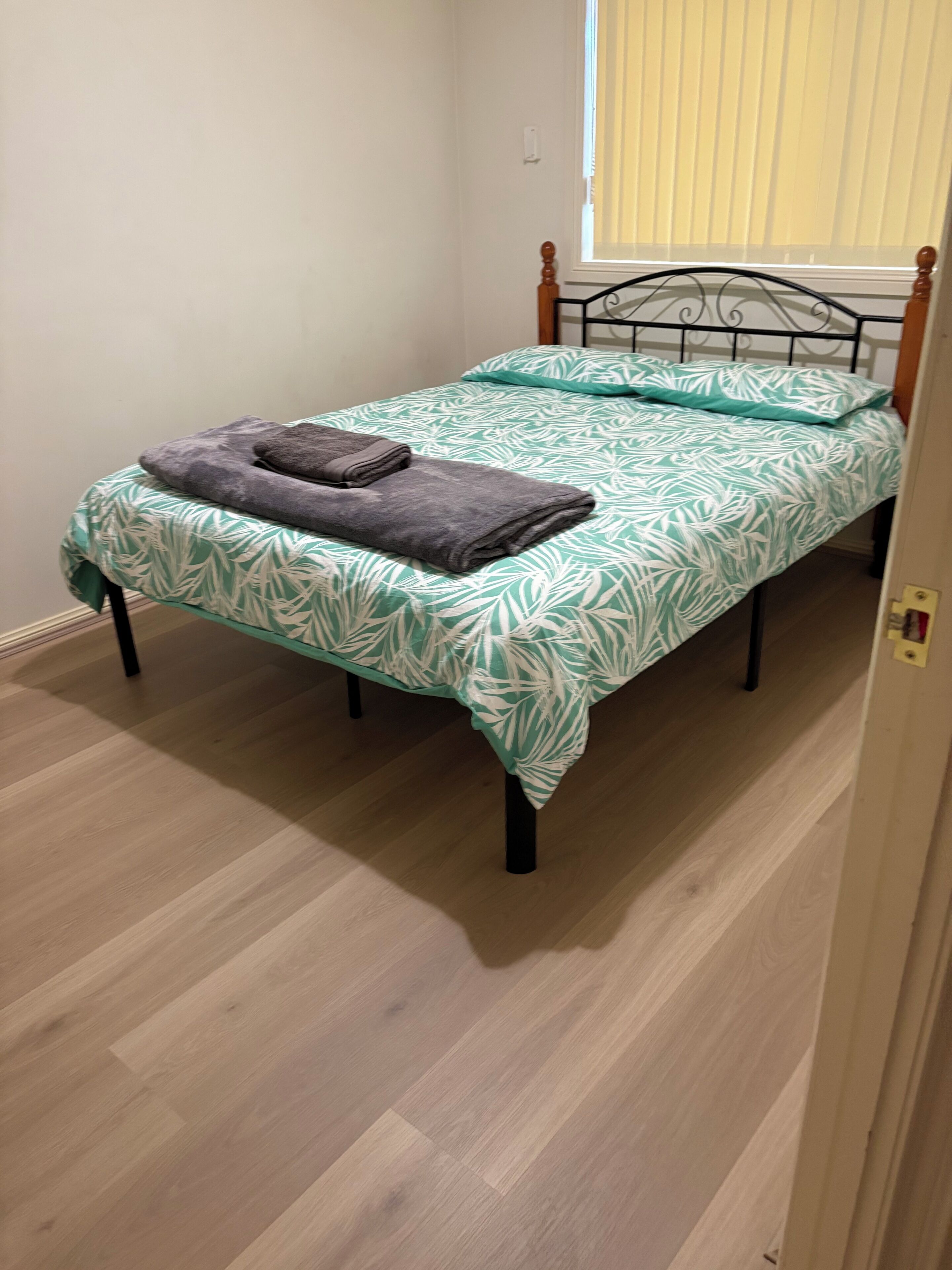 Un lit simple avec une couvre-lit à motifs, une serviette pliée et une fenêtre avec des stores.