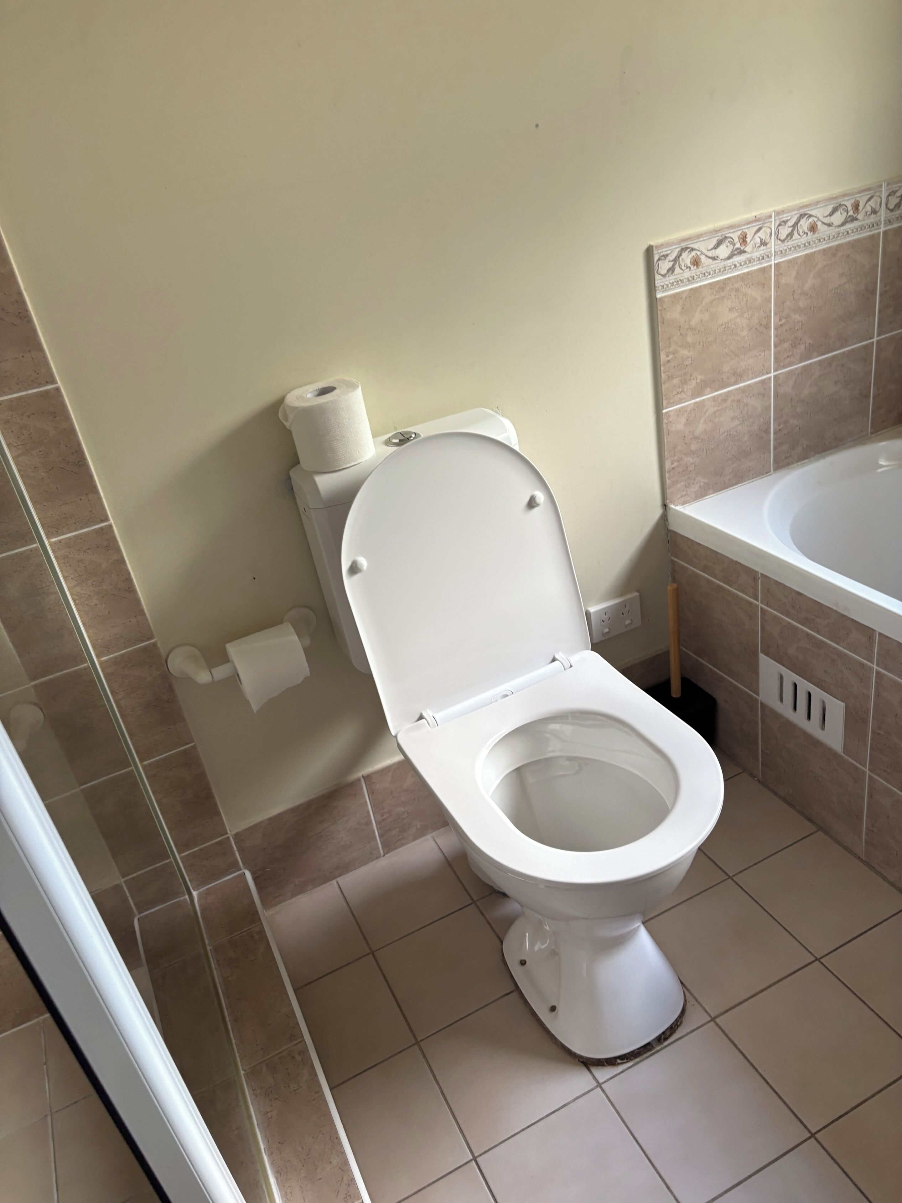A bathroom with a toilet, a roll of toilet paper, and a bathtub.