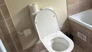 A bathroom with a toilet, a roll of toilet paper, and a bathtub.