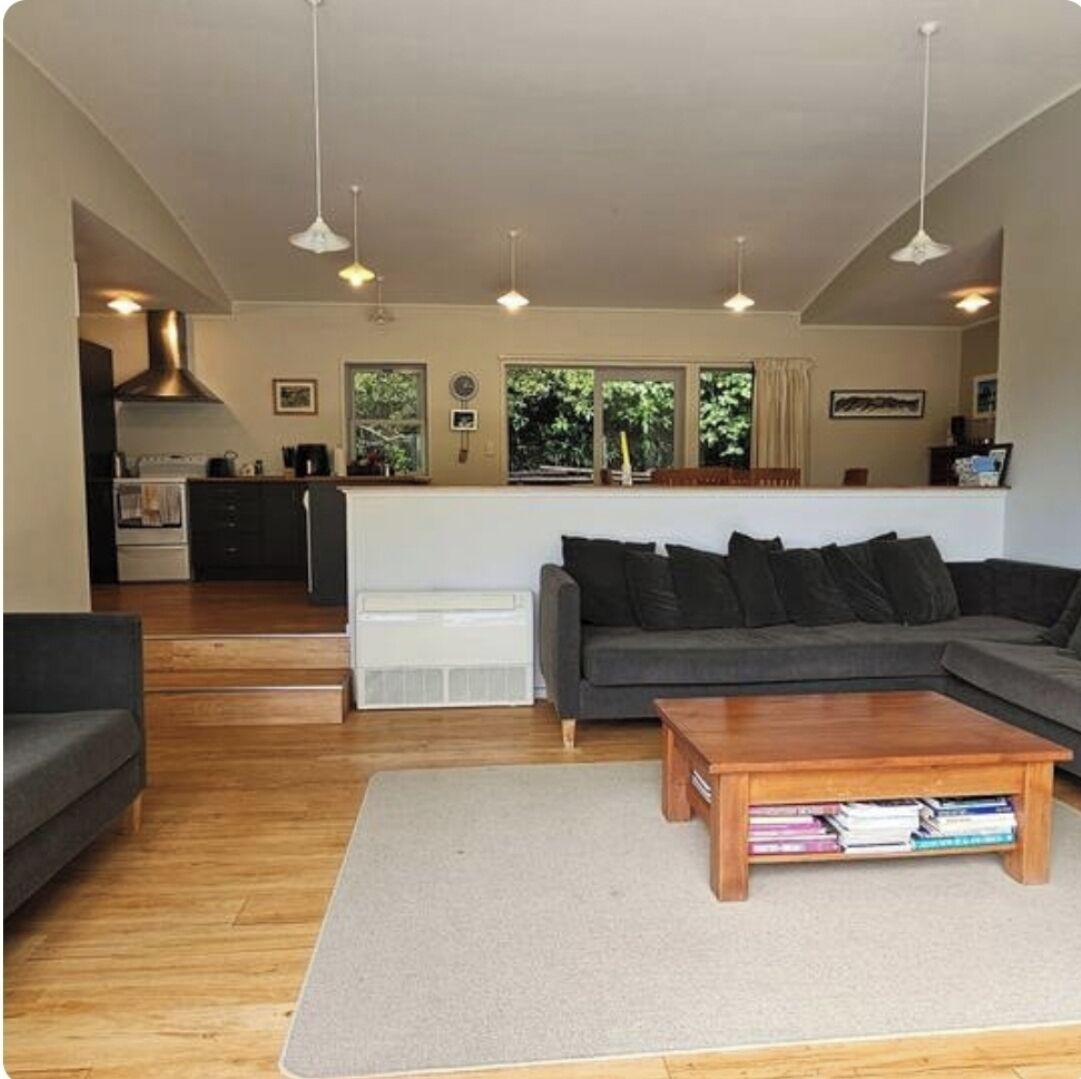A living room with a sofa, coffee table, and a kitchen in the background.