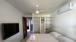 A hotel room with a bed, a TV, a ceiling fan, a wardrobe, and an air conditioning unit. - House 6 minutes walk from Point de Itaúna - Saquarema (Saquarema)