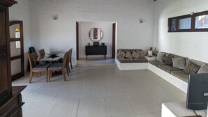 A spacious living area with a dining table, chairs, a sofa, and a television. - House 6 minutes walk from Point de Itaúna - Saquarema (Saquarema)