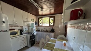 A kitchen with white cabinets, a dining table with woven placemats, and a red kettle on the shelf. - House 6 minutes walk from Point de Itaúna - Saquarema (Saquarema)
