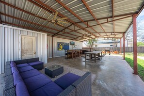 Un patio cubierto con mobiliario exterior, una televisión y una puerta.
