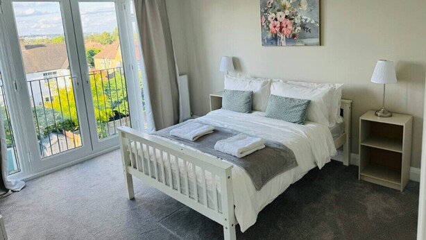 Ein Schlafzimmer mit einem Bett, zwei Nachttischen, einem Gemälde und Blick durch eine Schiebetür.