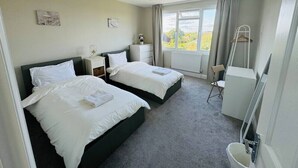 Ein Hotelzimmer mit zwei Betten, einem Schreibtisch, einem Stuhl, einem Heizkörper und einem Fenster mit Vorhängen.