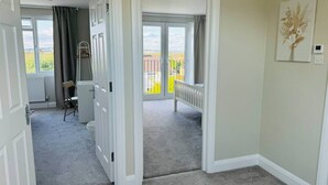 Ein Flur, der zu einem Balkon mit Aussicht führt, eine Tür mit Kleiderhaken und ein Gemälde an der Wand.