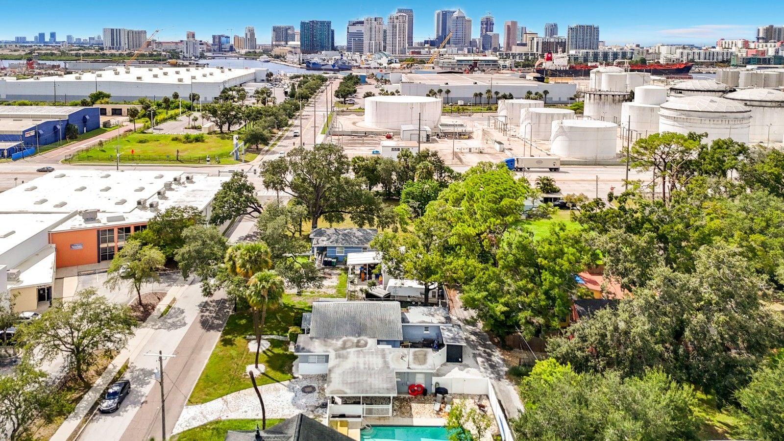 A residential area with a large industrial complex in the background, a swimming pool, and a clear view of the city skyline.