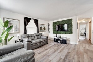 A modern living room with a grey leather sofa, a flat-screen TV mounted on a green wall, and a wooden floor. - Private Tampa Home Quick Drive to Attractions (Tampa)