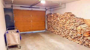 Een garage met een gesloten deur, een houtstapel en een metalen kar.