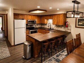 A kitchen with wooden cabinets, a stainless steel refrigerator, a microwave, an oven, a sink, and a bar area with stools. - Cozy Mountain Retreat in the heart of McCall (McCall)