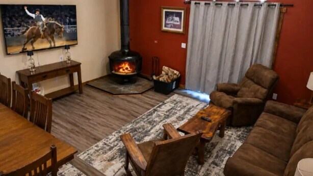Een woonkamer met een open haard, een aan de muur bevestigde televisie, een bank, een salontafel en een eethoek met stoelen.