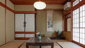 Una tradizionale stanza giapponese con pavimento in tatami, un tavolo in legno, una lampada a sospensione, porte scorrevoli e un'ampia brocca.