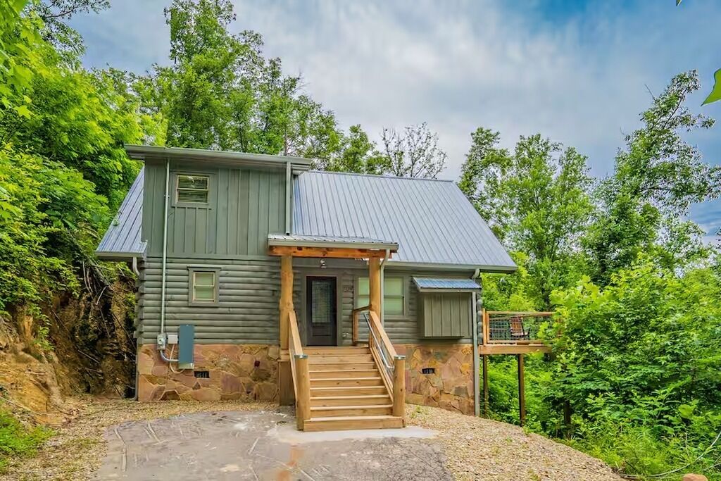 A log cabin with a wooden staircase leading to a front door, surrounded by trees.