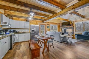 Eine geräumige Küche mit Holzbalken, ein Essbereich mit einer Bank und ein Wohnzimmer mit Sofa und blauem Sessel.
