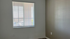 Una habitació amb ventilador de sostre, finestra amb persianes i terra de fusta.
