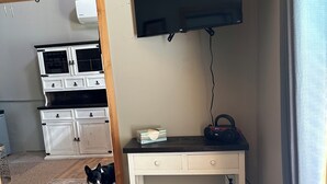 Ein Wohnzimmer mit einer Couch, einem Couchtisch, einem an der Wand befestigten Fernseher, einem Schrank und einem Hund.