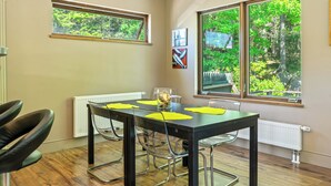 A dining area with a table, chairs, and a view of greenery outside. - The Crag: On the Acadia National Park Border - Deck, Fire Pit, Steps to Trails (Mount Desert)