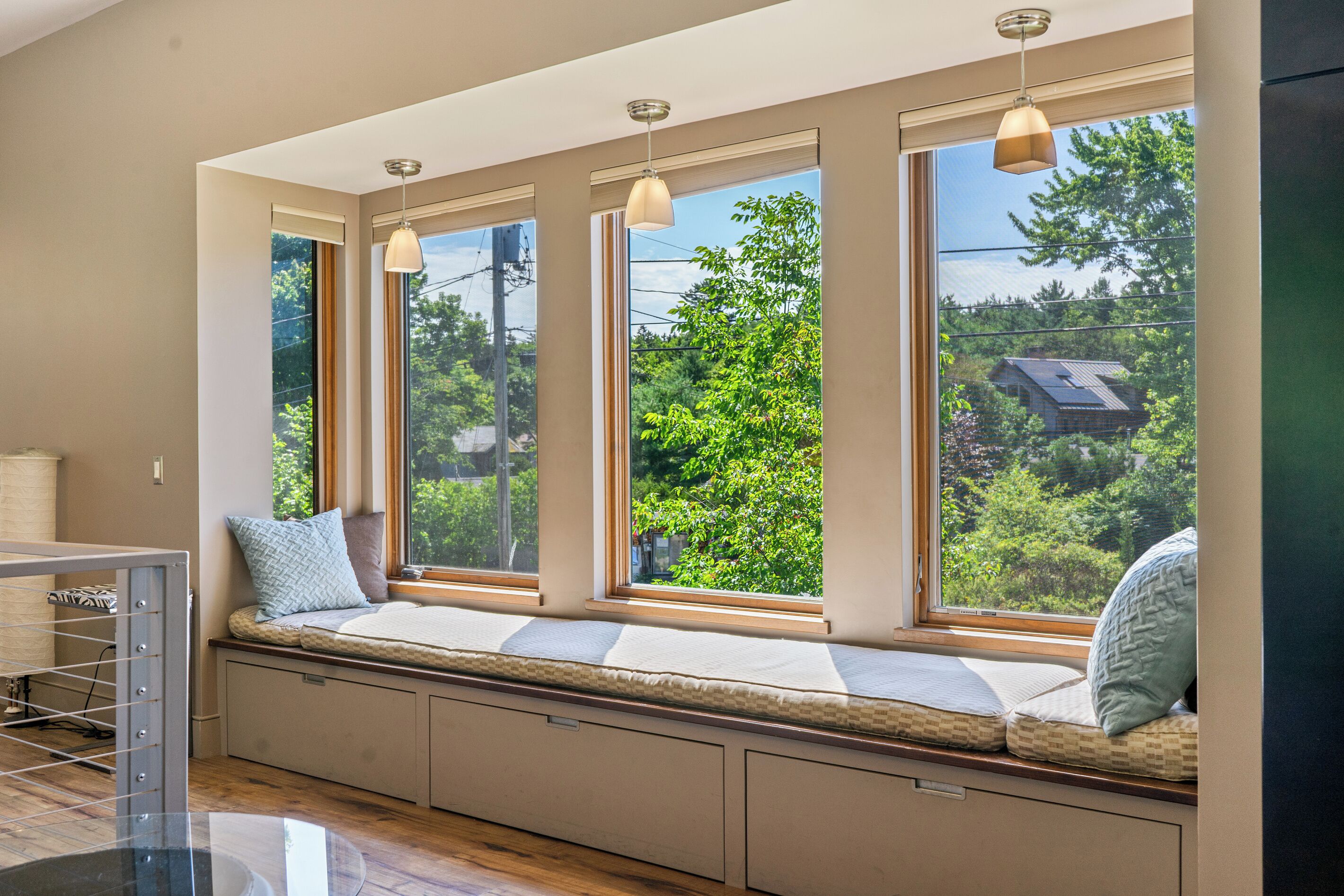 Ein Zimmer mit einer eingebauten Sitzbank an einem großen Fenster mit mehreren Scheiben, das einen Blick ins Grüne bietet.