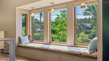 Ein Zimmer mit einer eingebauten Sitzbank an einem großen Fenster mit mehreren Scheiben, das einen Blick ins Grüne bietet.