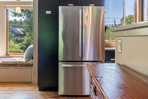 Une cuisine équipée d’un réfrigérateur en acier inoxydable, d’un plan de travail en bois et d’une fenêtre donnant sur un paysage verdoyant.