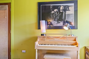 Un pianoforte con finitura in legno e un leggio, posizionato di fronte a una parete gialla con un'opera d'arte incorniciata sopra.