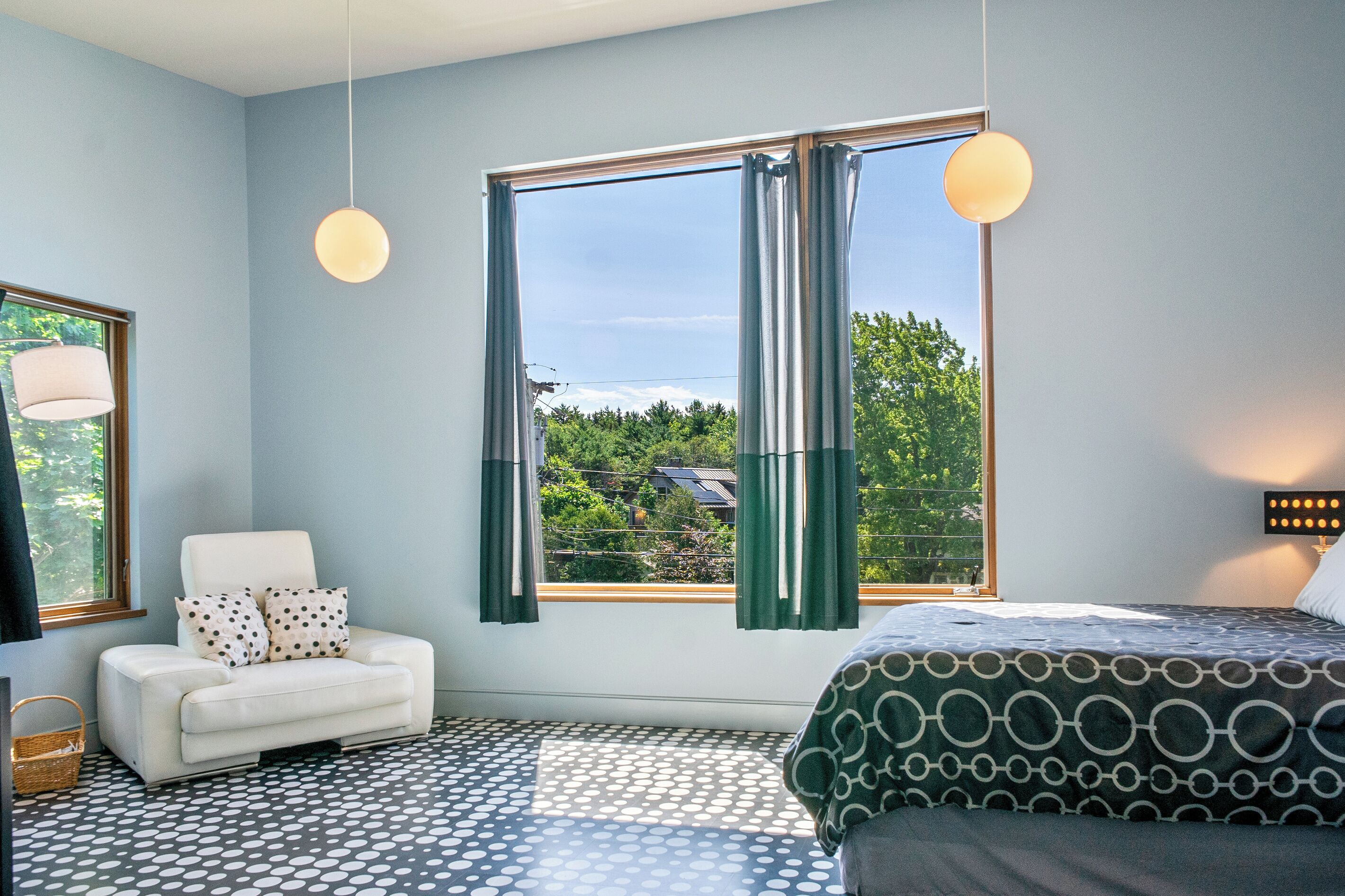 A bedroom with a bed, a chair, a window with curtains, and a patterned floor.