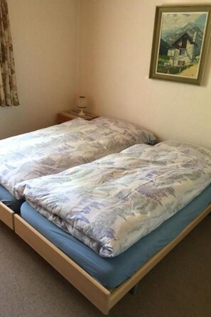 Ein Doppelbett mit floralem Überwurf, ein Nachttisch mit Lampe und ein gerahmtes Bild an der Wand.