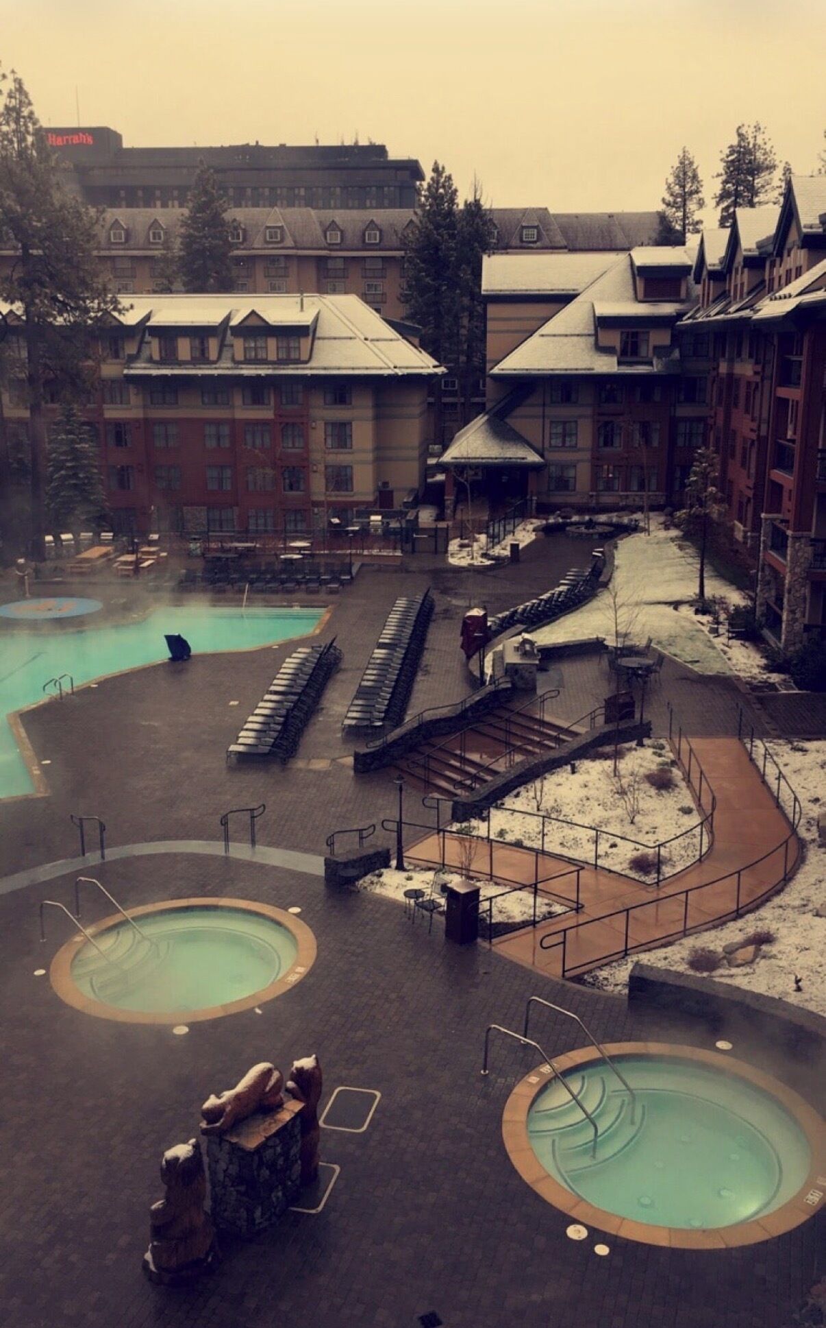 A resort with multiple swimming pools, a snow-covered landscape, and a building with a Harrah's sign.