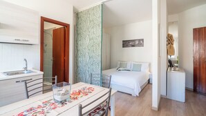 Una camera d'albergo compatta con angolo cottura, un letto con cuscini, un piccolo comodino e uno specchio.
