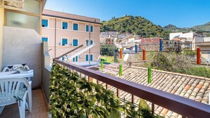 Un balcone con tavolo e sedie, vista su una cittadina collinare e un edificio con diverse finestre.