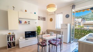 Un ambiente compatto con angolo pranzo, televisore, libreria e balcone con vista.