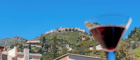 A view of a hillside with buildings, a clear blue sky, and a glass of red wine.