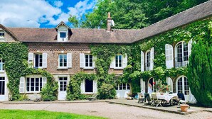 Un grand bâtiment en briques, recouvert de lierre, doté de nombreuses fenêtres et d’une cour intérieure aménagée avec des sièges.