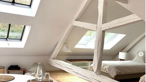Une chambre à coucher aménagée dans un espace en hauteur, avec des fenêtres de toit, un lit, une table de chevet et un petit coin bureau.