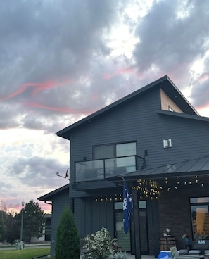 A modern two-story house with a balcony, a flag, and string lights.