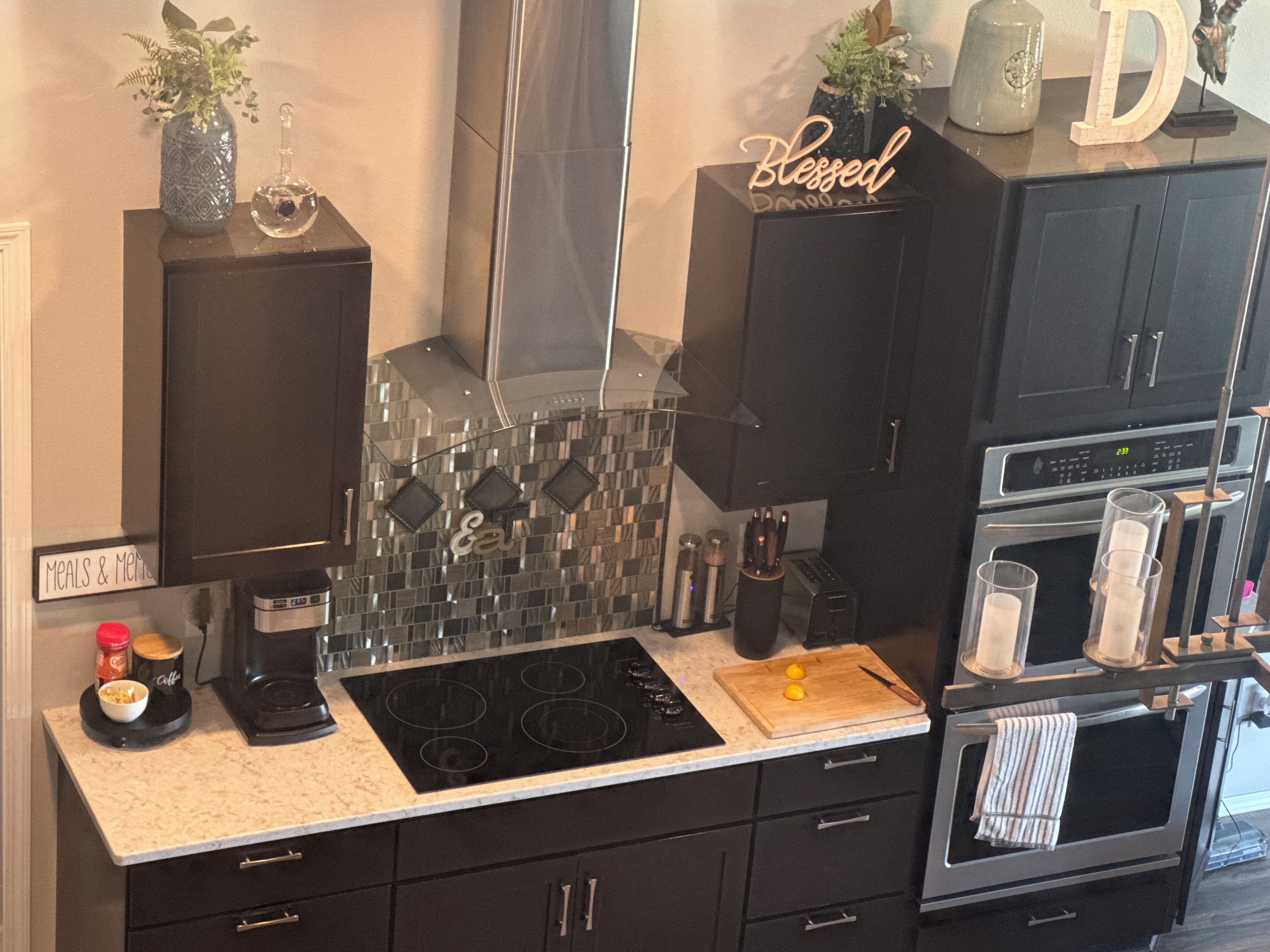 A modern kitchen with a black countertop, a stove, and a microwave. There are cabinets, a coffee maker, and a sign that reads 'Meals & Menu.'
