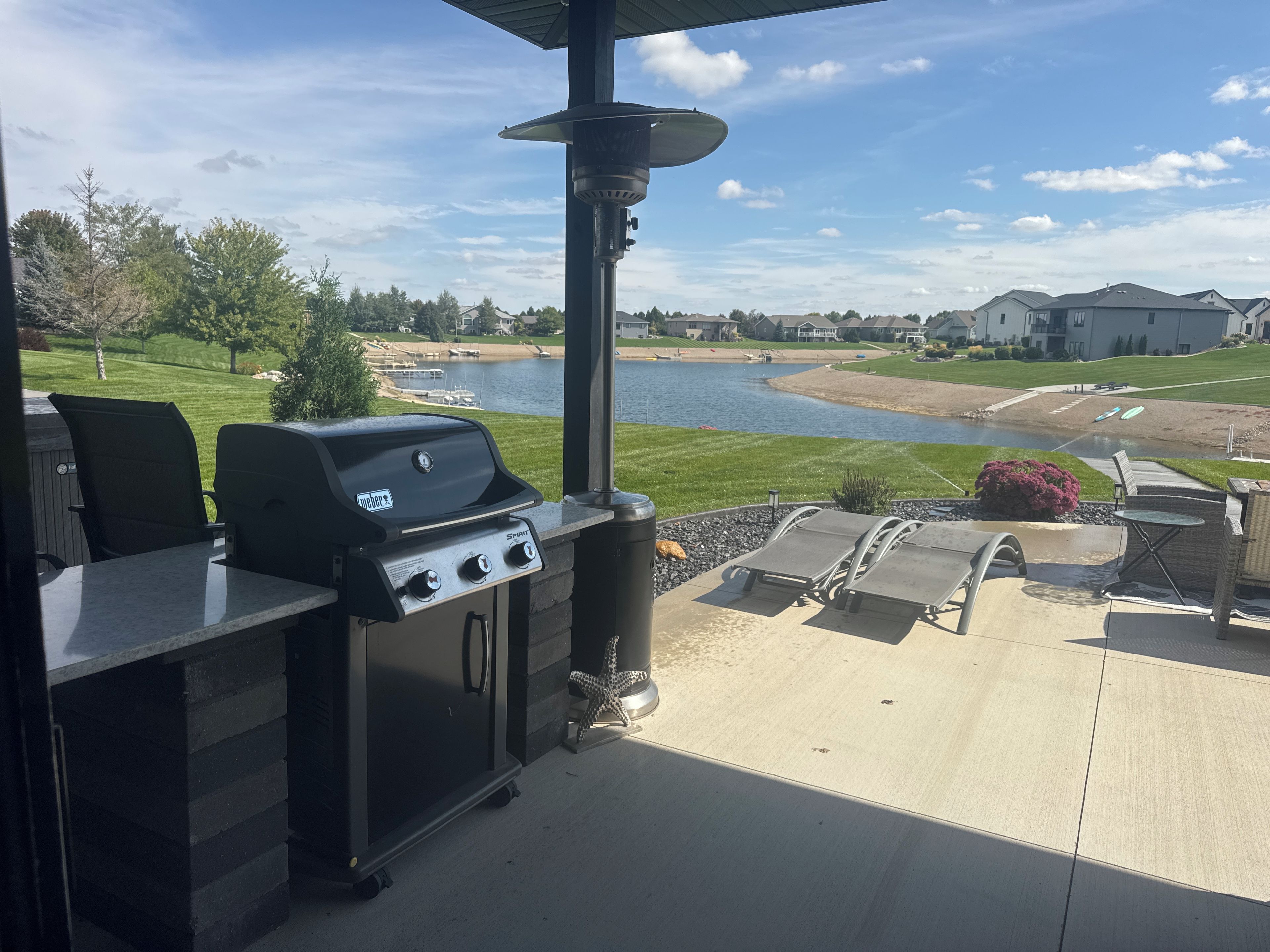 Une terrasse extérieure équipée d’un barbecue, de sièges et offrant une vue sur un lac et des maisons.