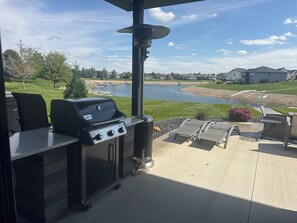 An outdoor patio with a grill, seating, and a view of a lake and houses.