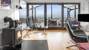 Een moderne woonkamer met een grote glazen deur die leidt naar een balkon, een zwarte leren fauteuil, een open haard en een telescoop.