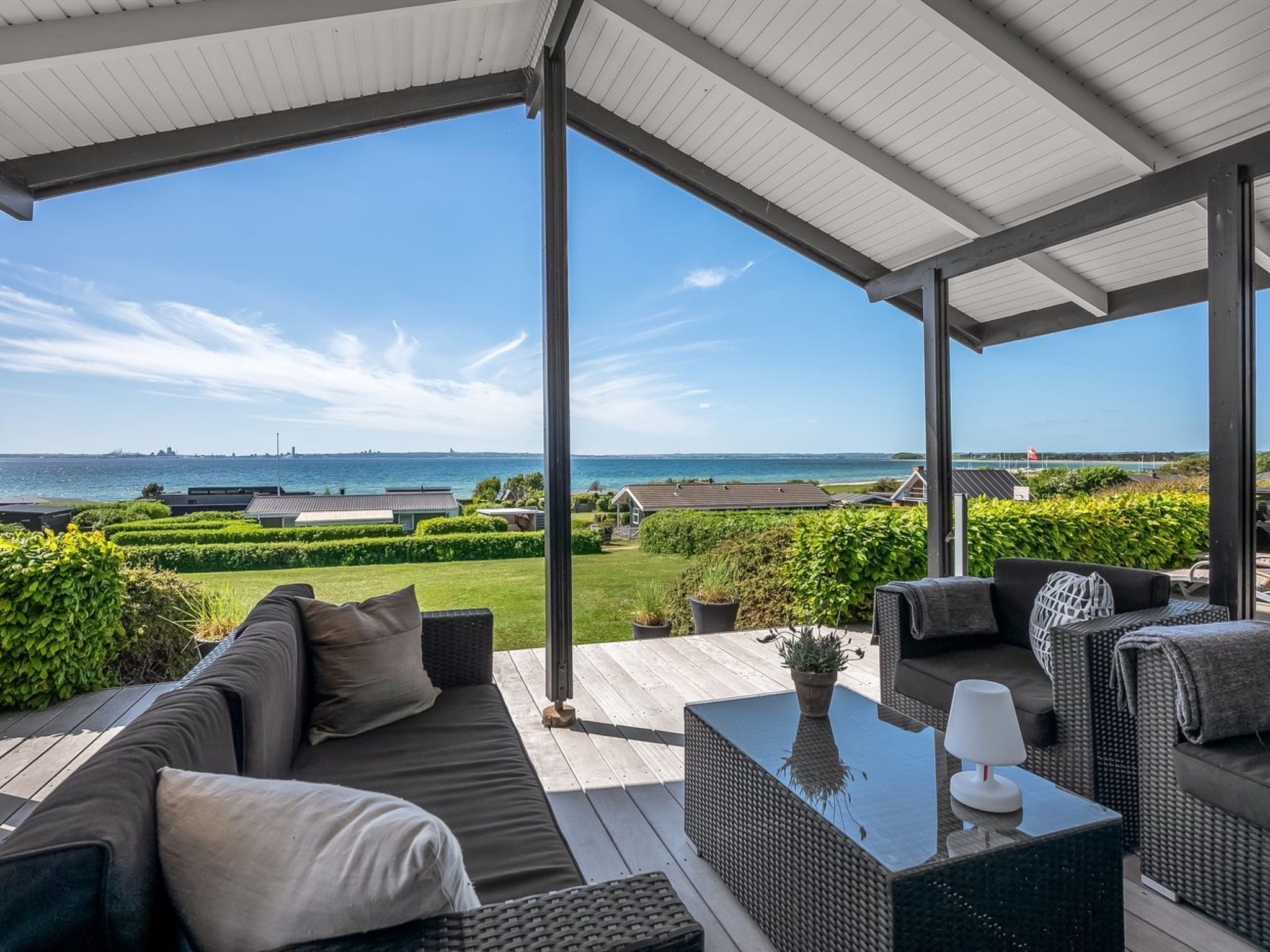 A covered outdoor seating area with a view of the sea and a distant city skyline.
